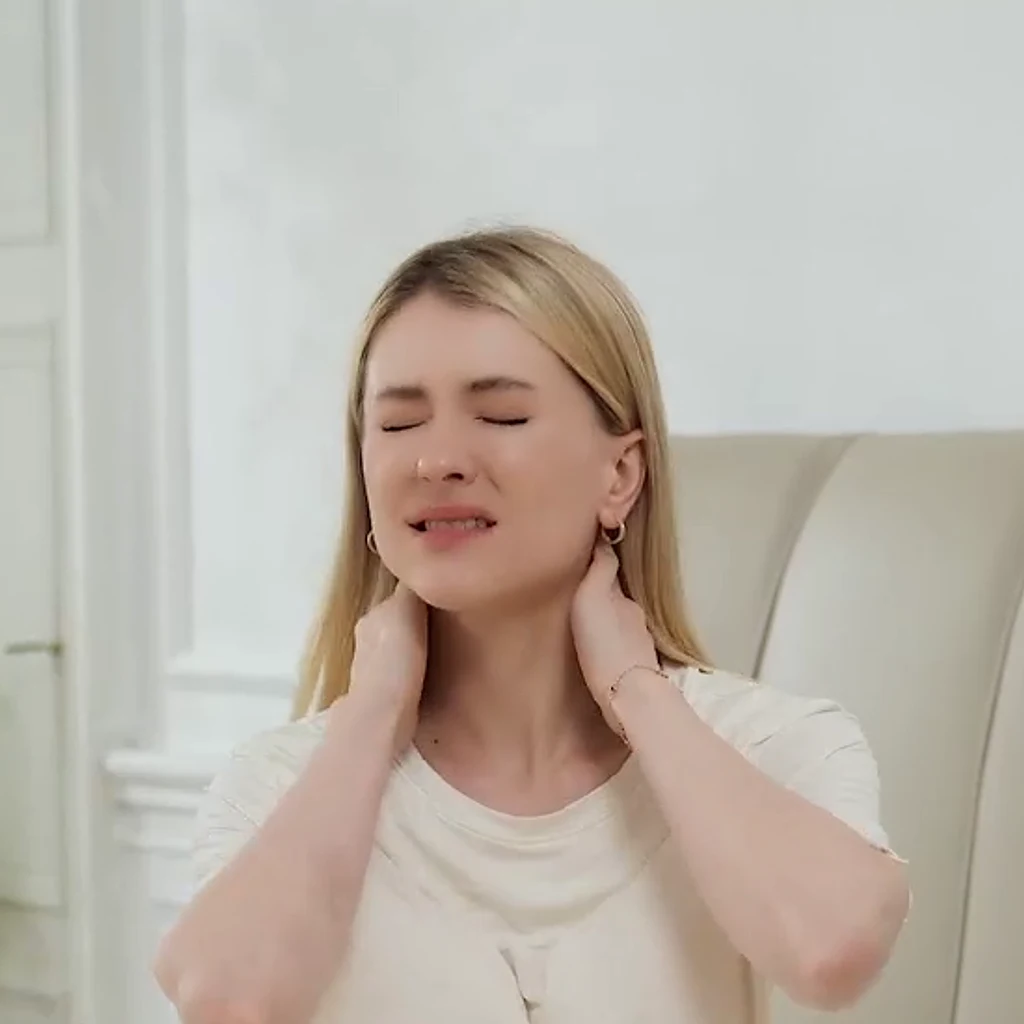 Žena sedí na posteli s rukami na krku